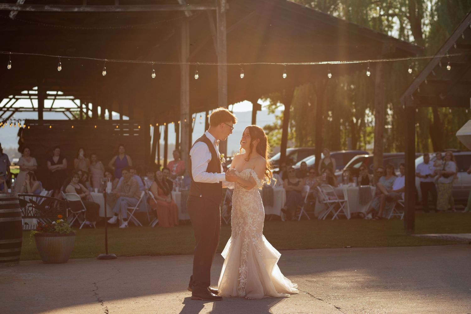 Bride and groom share first dance outdoors at golden hour wedding reception with guests seated in background.