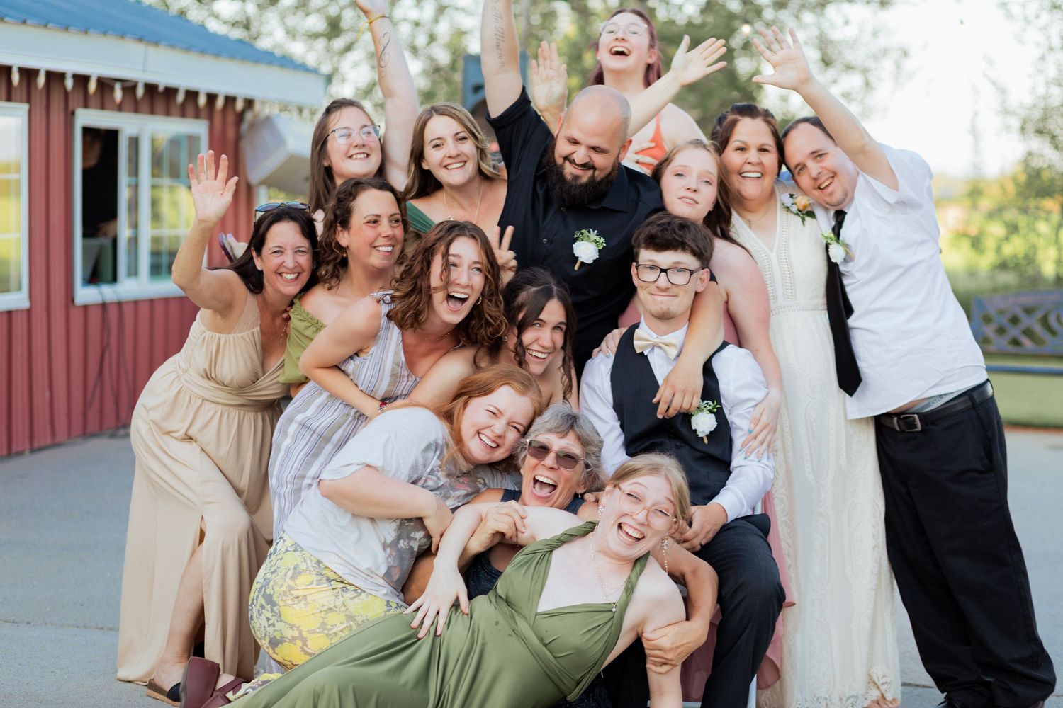 Joyful wedding group photo with bride, groom, and guests celebrating outdoors near a red barn.