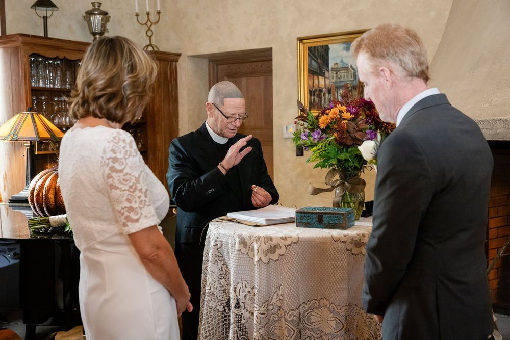 Officiant reads from book during intimate wedding ceremony at a rustic venue with colorful floral arrangement.