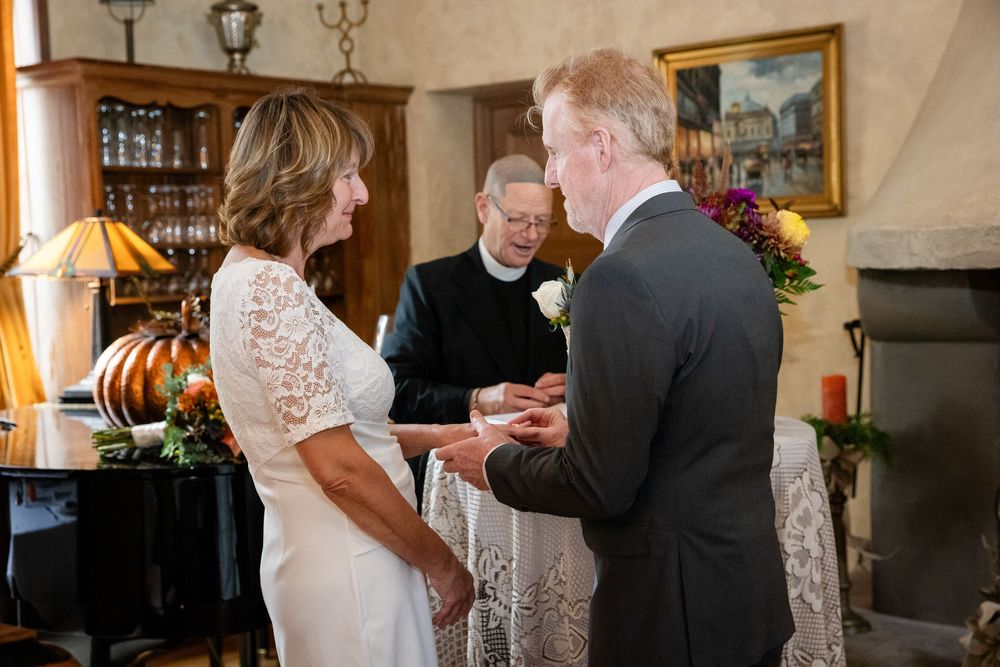 Couple exchanging wedding rings during intimate ceremony with officiant in elegant wood-paneled room.
