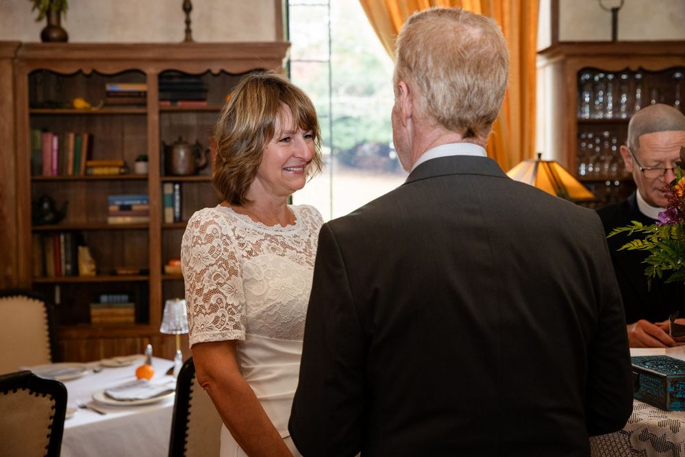 Smiling bride in lace dress holding grooms hands during intimate wedding reception.