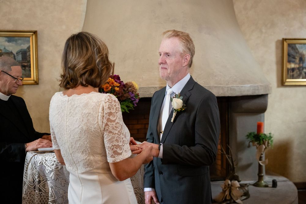 Groom in dark suit holding brides hands during heartfelt wedding vow exchange indoors.