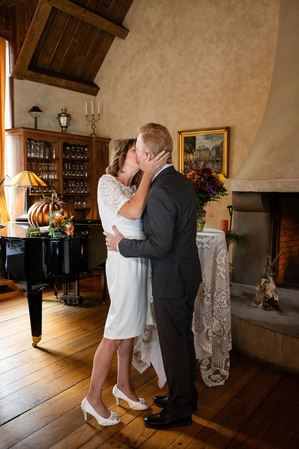 Newlyweds sharing first kiss as married couple beside fireplace in rustic elegant venue.
