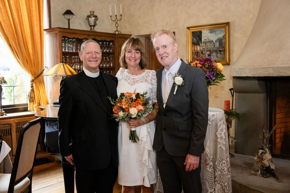 Bride holding orange bouquet posing with groom and officiant after intimate wedding ceremony.