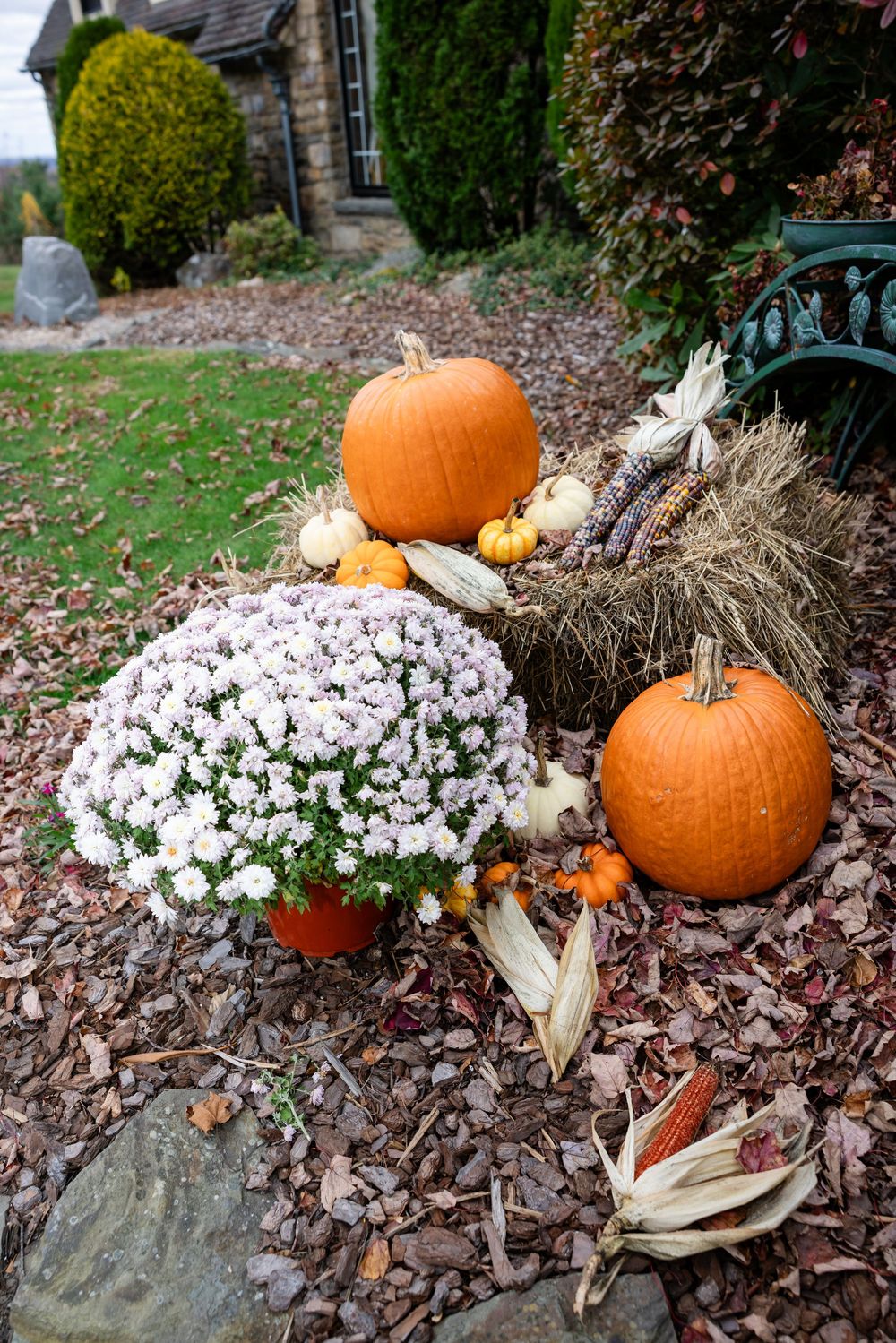 Fall wedding decor featuring orange pumpkins, white mums, hay bales, and dried corn outside a venue.
