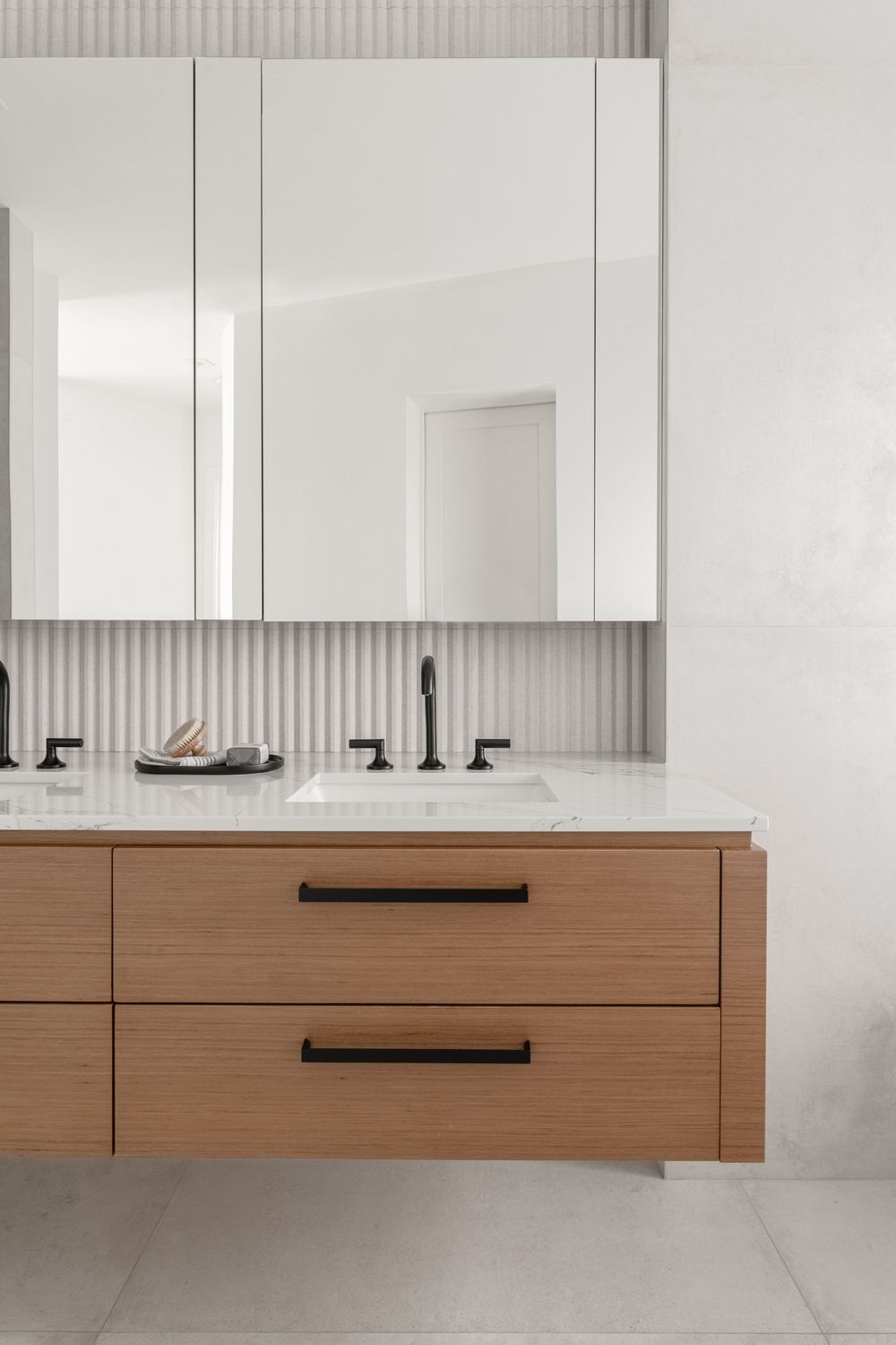 Floating wood vanity with black hardware, marble countertop, dual sinks, and mirrored medicine cabinet in modern bathroom.