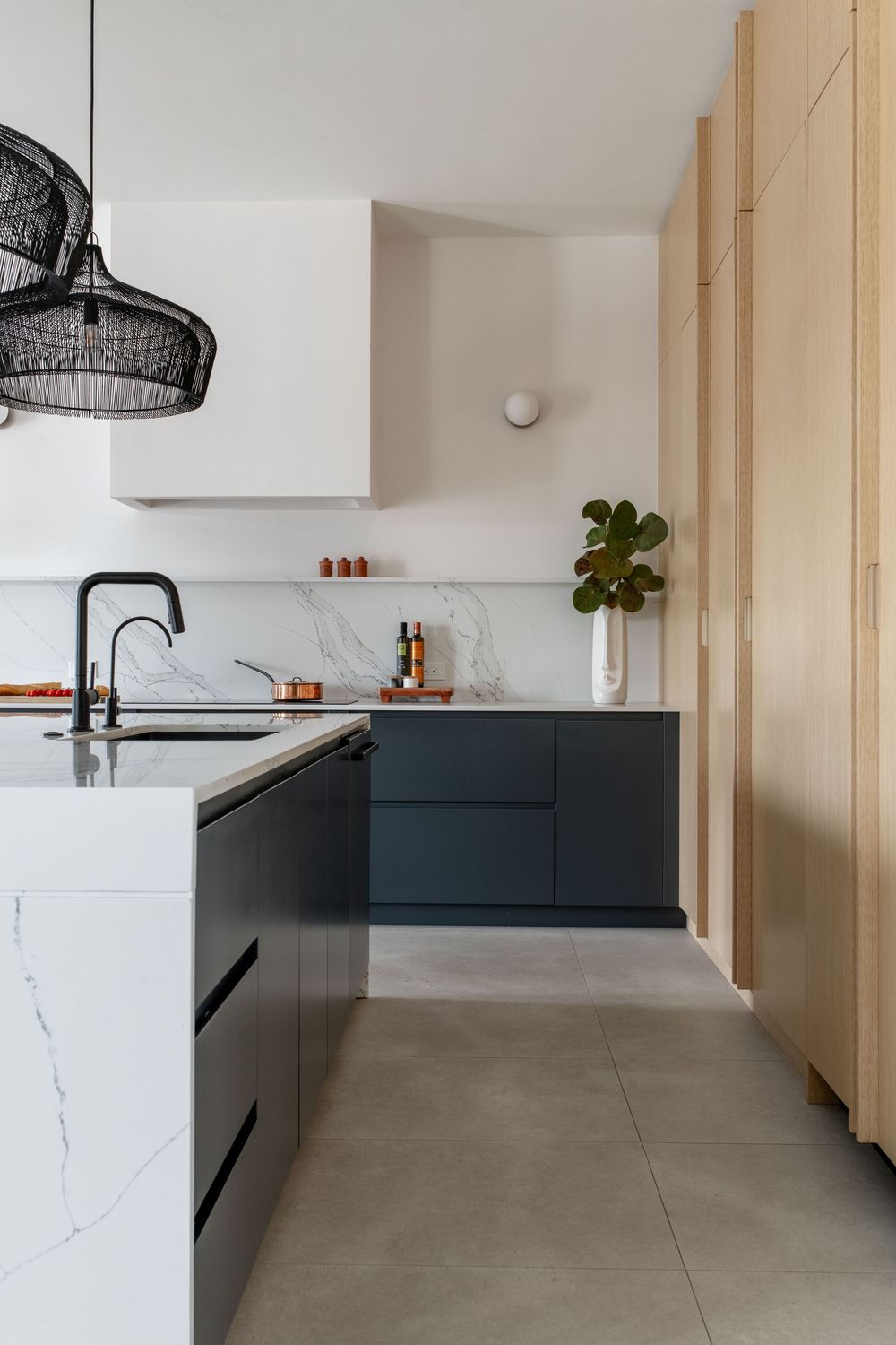 Sleek kitchen with dark navy cabinets, marble backsplash, black fixtures, concrete floors, and natural wood tall cabinet storage.
