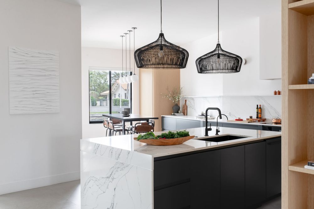 Modern kitchen with marble island, black cabinetry, pendant lights, and open living area with natural light.