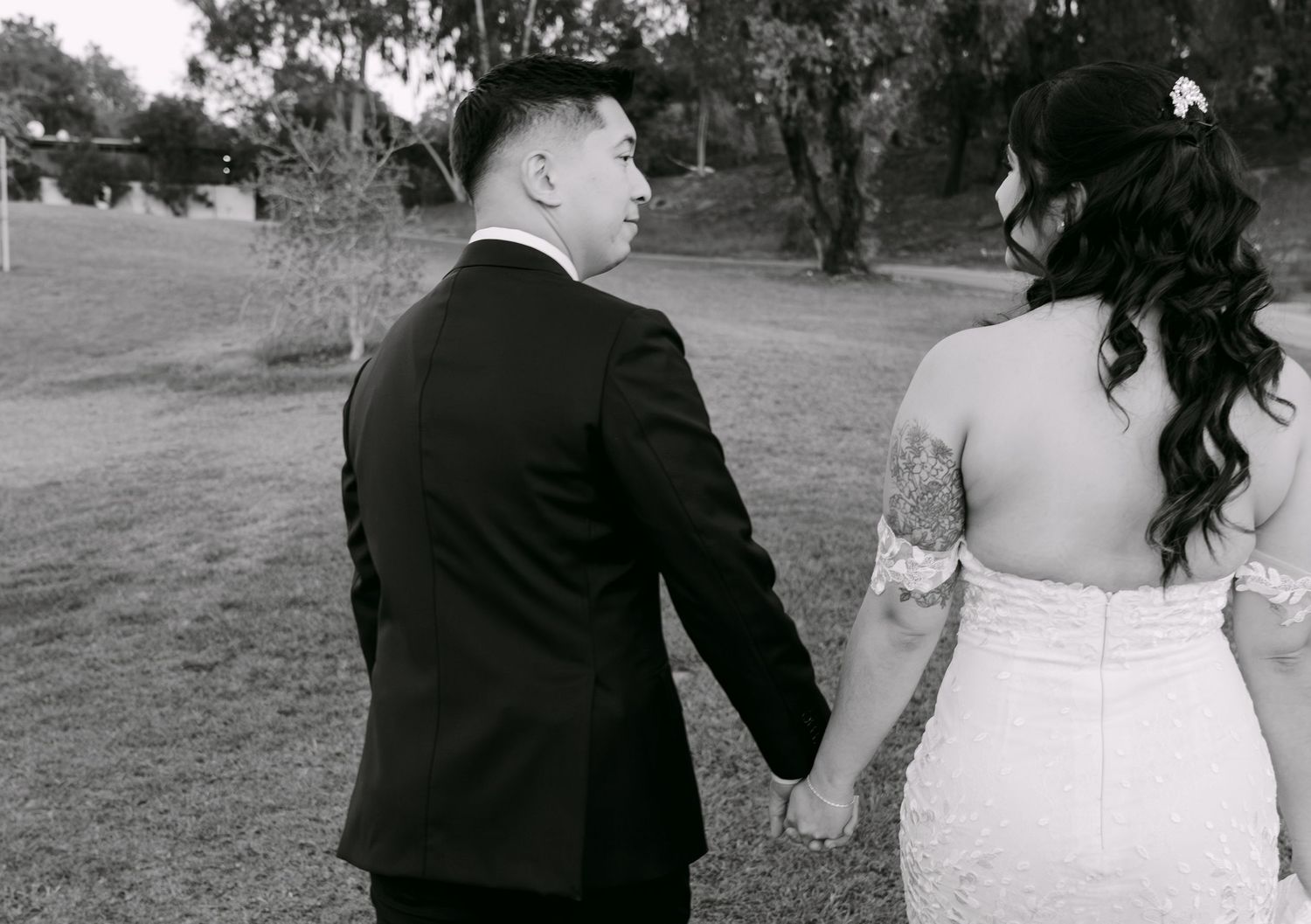 Black and white photo of a bride and groom holding hands walking outdoors on their wedding day.
