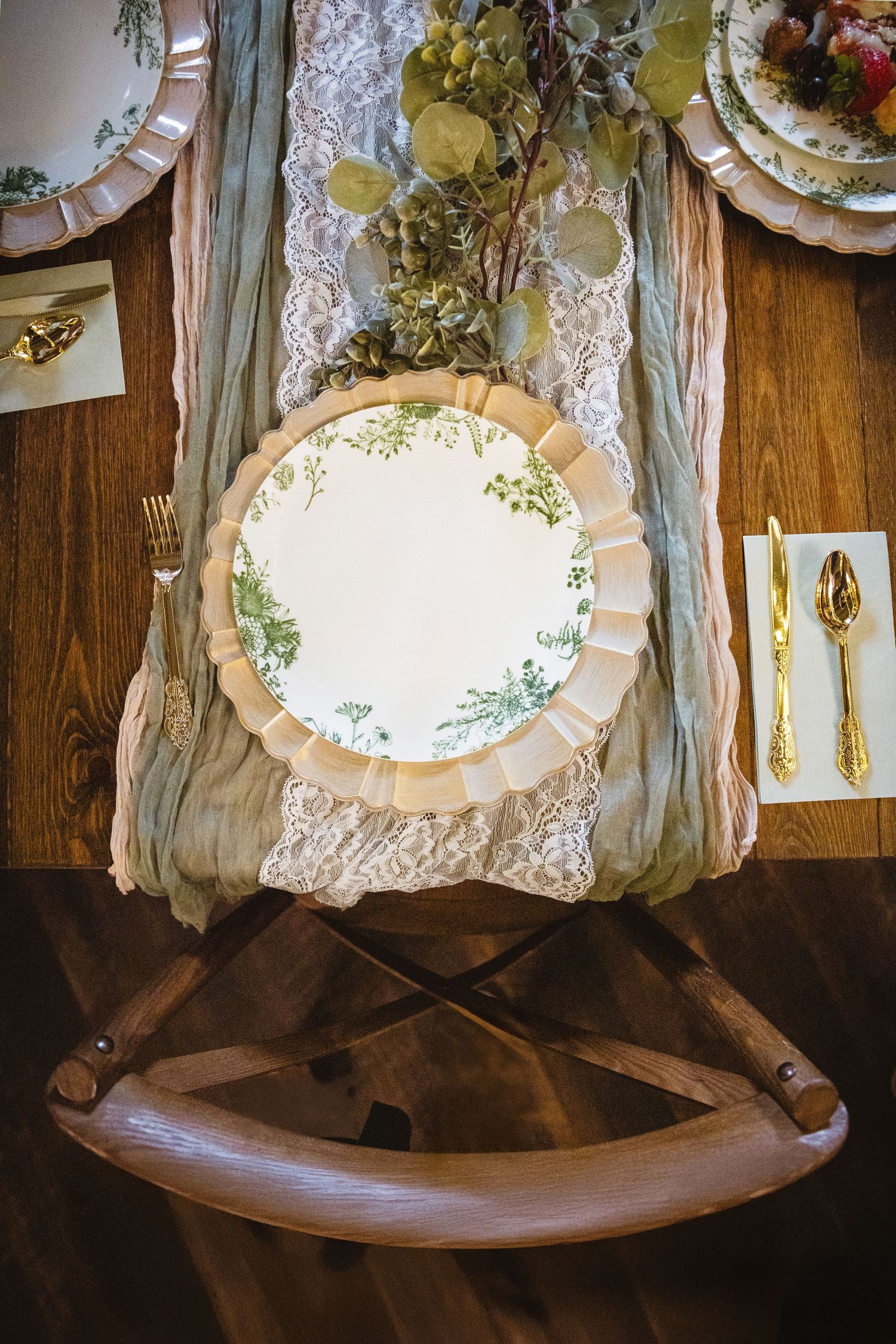 Elegant table setting with lace runner, white china plates, and gold flatware on dark wooden surface creates vintage charm.