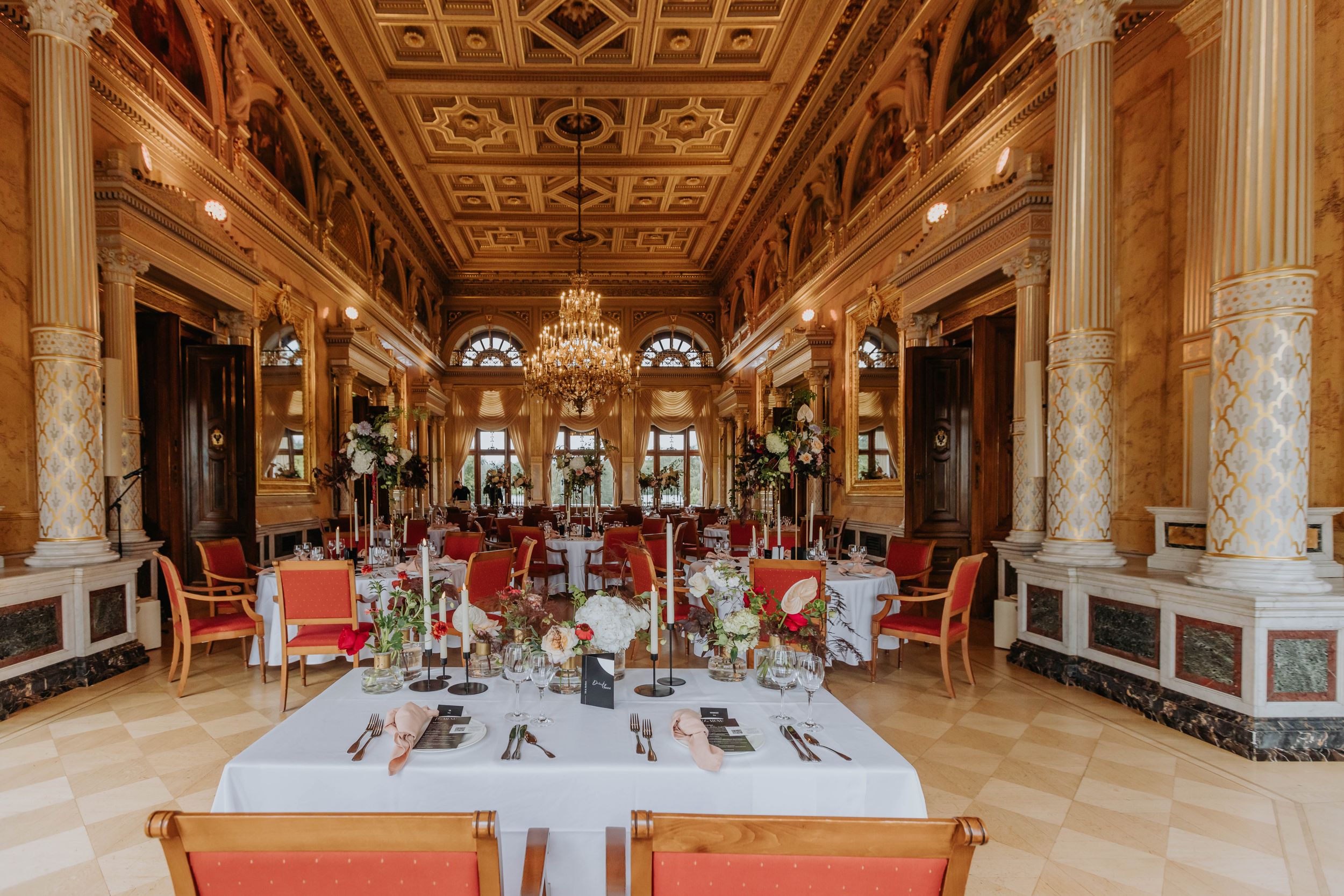 Panoramic view of an ornate grand ballroom with crystal chandeliers, gilded columns and elegant dining tables.