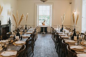 Rustic wedding reception table setup with dried pampas grass and place settings in a bright white room with wooden floors at Aswarby Rectory