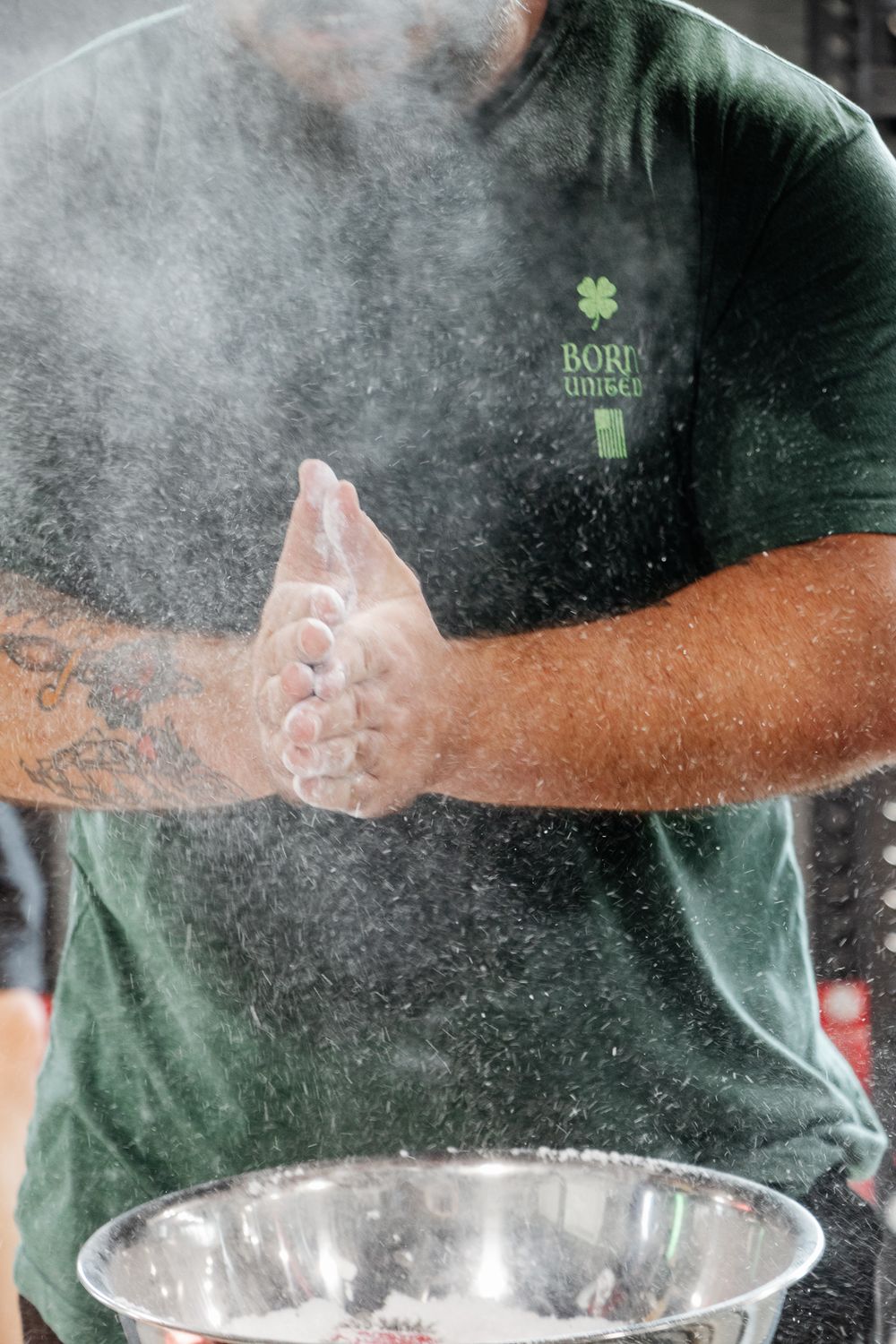 Close-up of man in green shirt clapping chalked hands, creating a dramatic cloud of chalk dust before lifting
