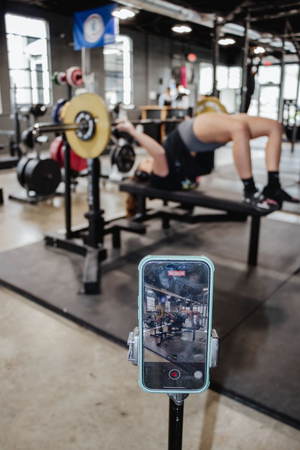 Phone on tripod records a woman performing a bench press in the gym, capturing her lift in real time