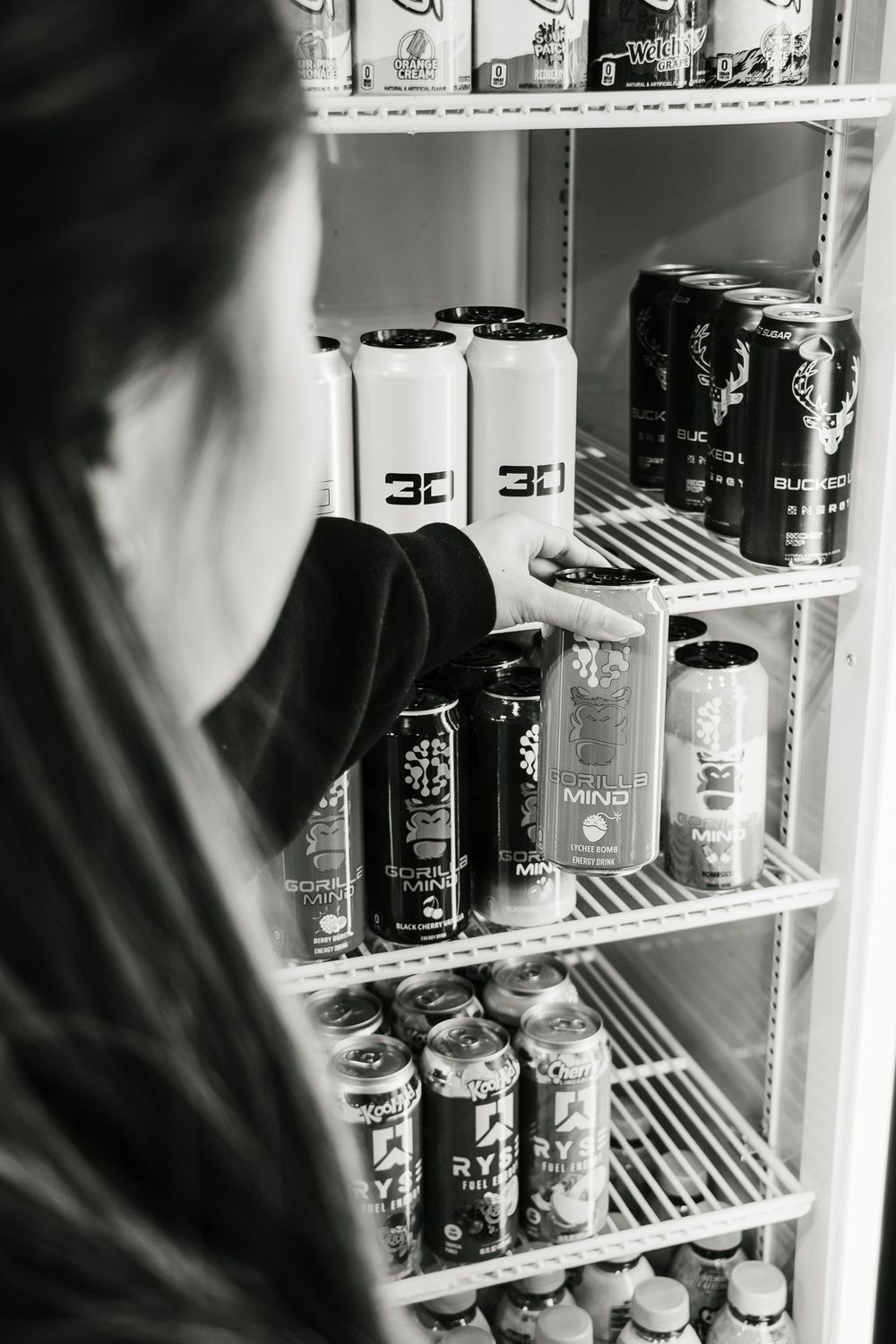 Woman reaches for a Gorilla Mind energy drink inside a gym fridge
