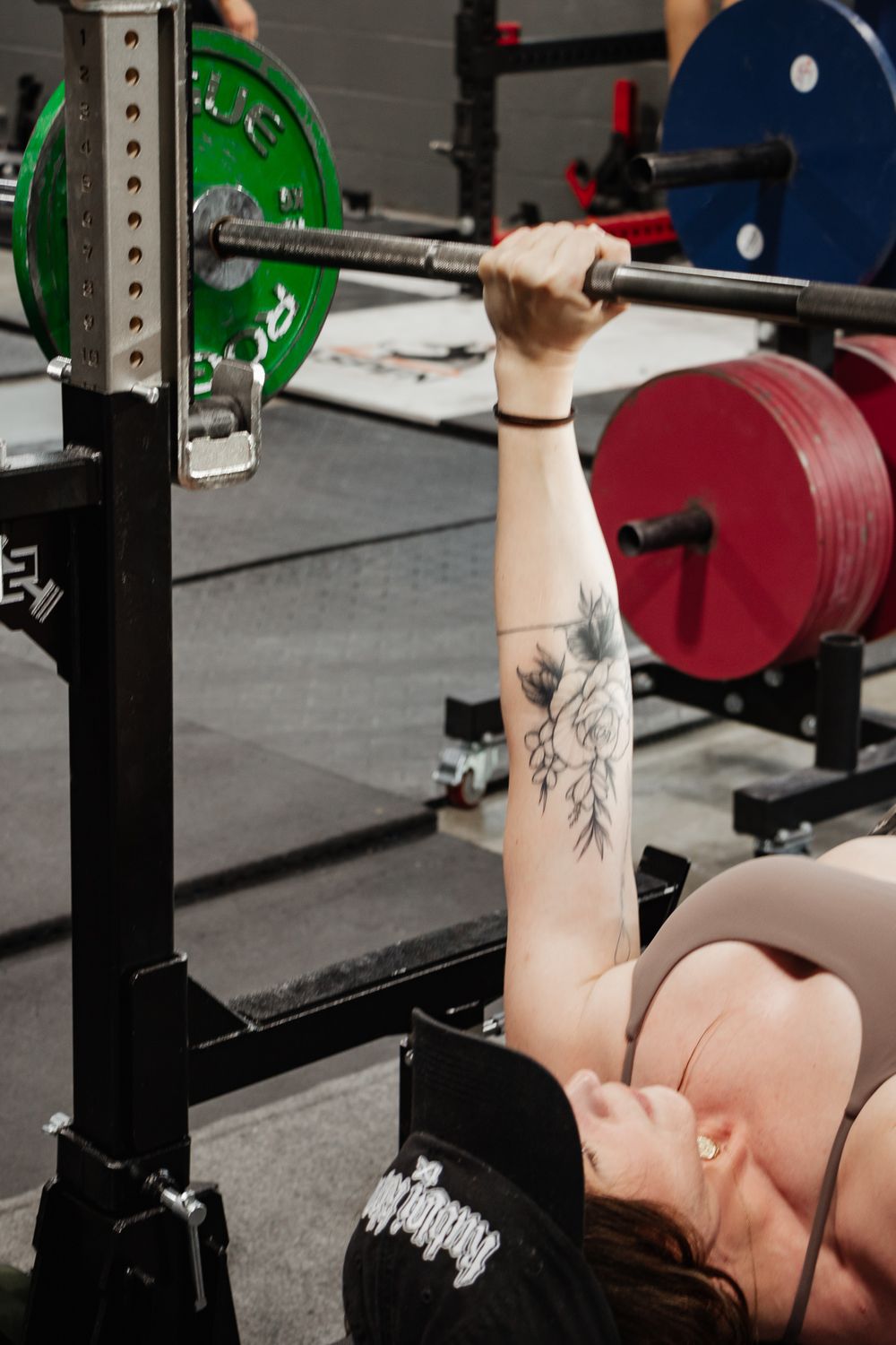 Woman bench pressing with green Rogue weight plates and tattooed arm