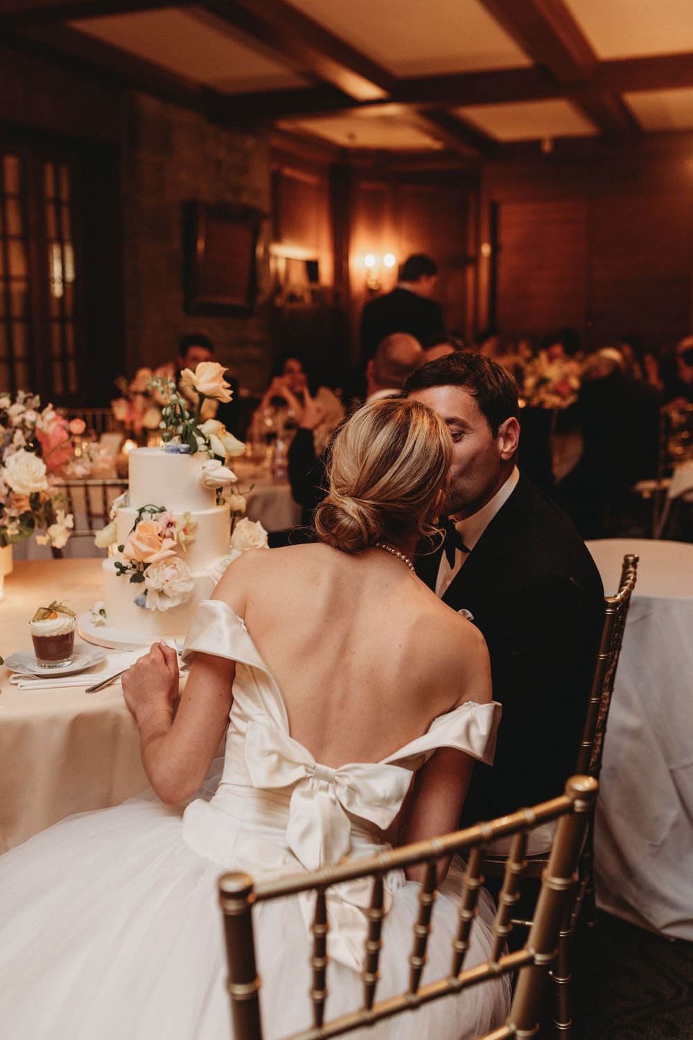Newlyweds share intimate moment at reception table with elegant white floral centerpiece and warm candlelit ambiance.