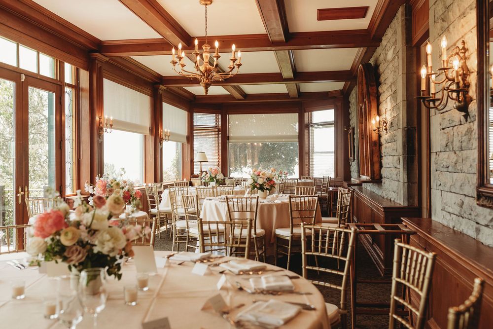 Elegant wedding reception room with wooden beams, chandeliers, stone walls and round tables set for a formal dinner.