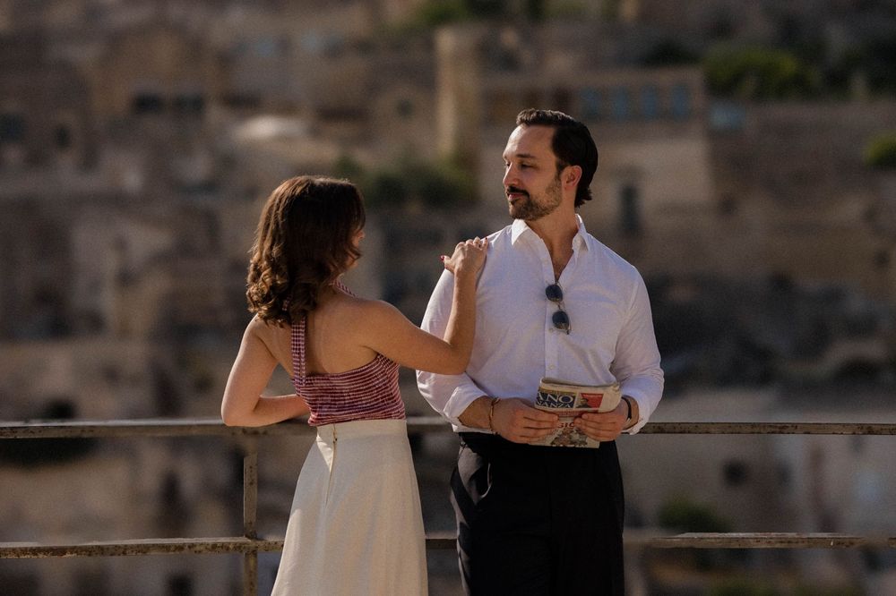 Couple in formal attire share romantic moment on balcony overlooking stone architecture during sunset.