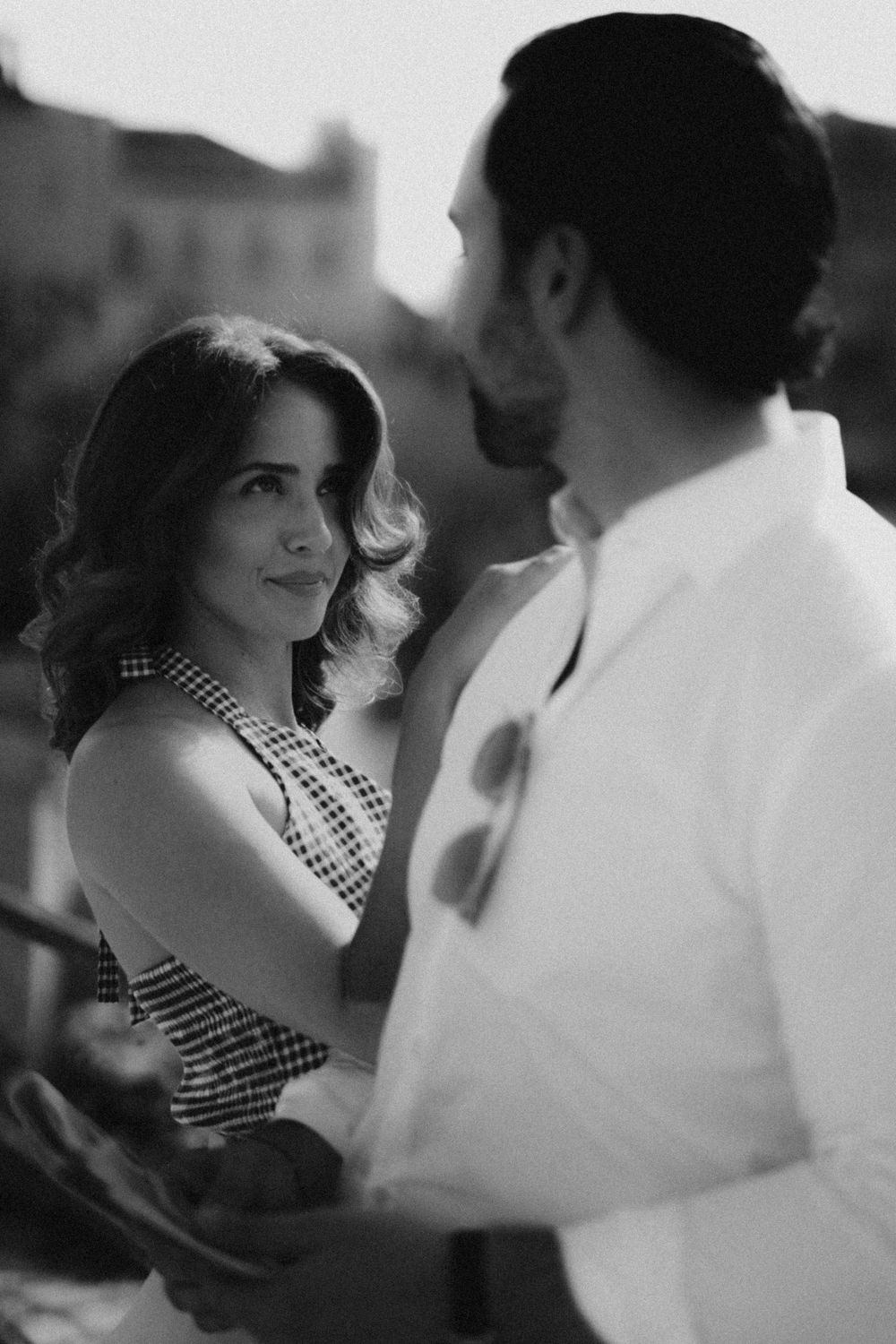 A couple shares an intimate black and white moment as they face each other, with her wearing a patterned dress.