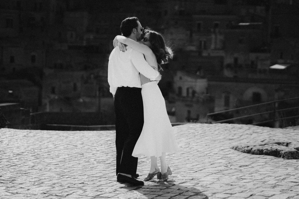 A couple shares an intimate embrace on a snowy winter landscape in black and white photography.