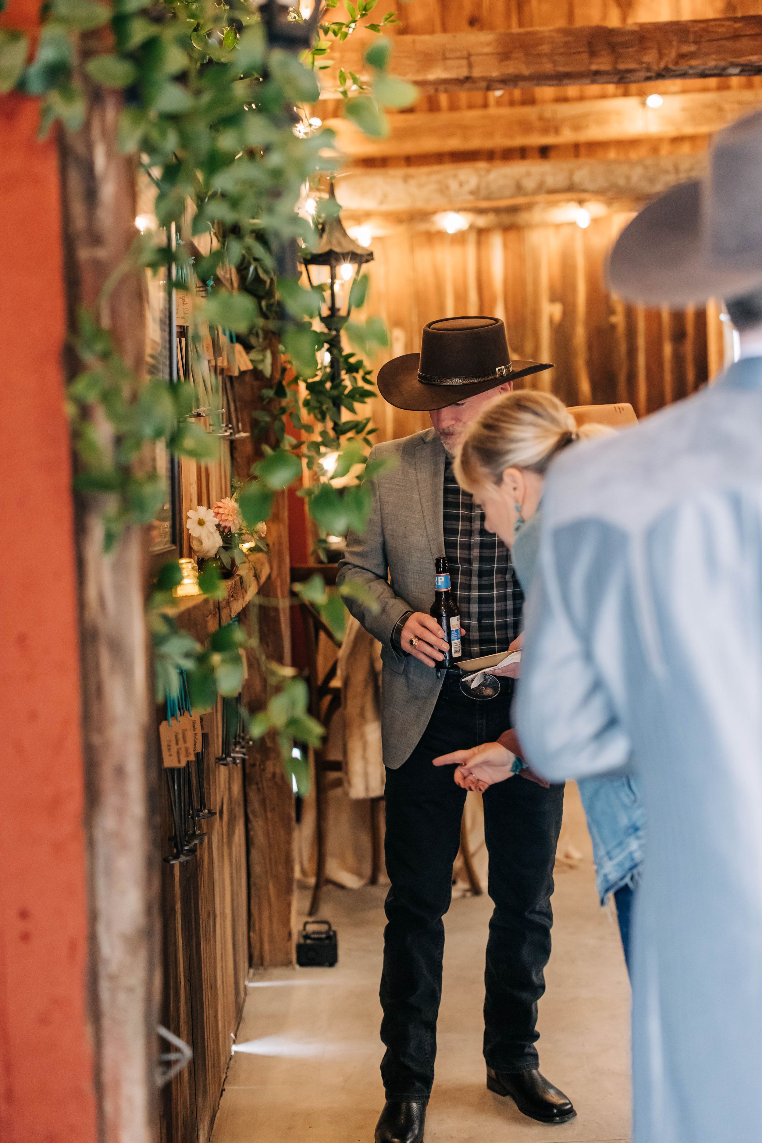 A rustic barn venue decorated for a wedding with string lights and greenery along wooden beams and posts.