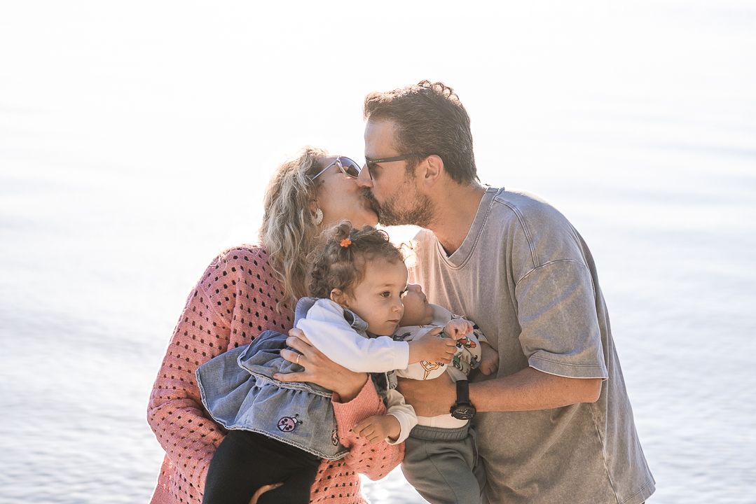 A tender family moment captured by the ocean as parents share a kiss while embracing their young child.