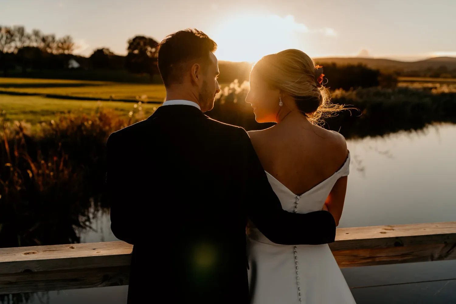 Silhouetted wedding couple against dramatic sunset over water landscape.