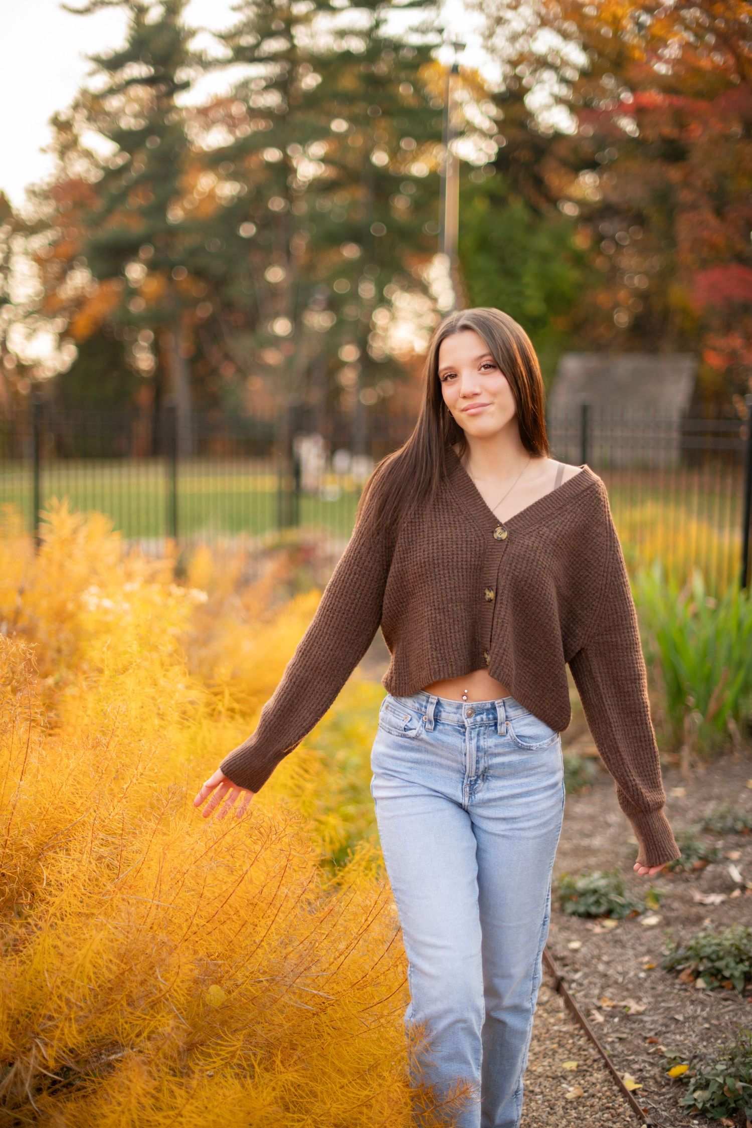 Person wearing brown cardigan and jeans poses against vibrant yellow autumn foliage in outdoor setting.