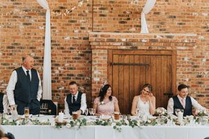 Wedding party members seated at a rustic head table with exposed brick wall at Hall Farm - image captured by Grimsby photographers.
