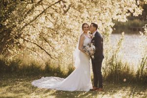 A romantic wedding couple embraces under golden sunlit trees during their outdoor ceremony at Hall Farm - image by Grimsby photographers.