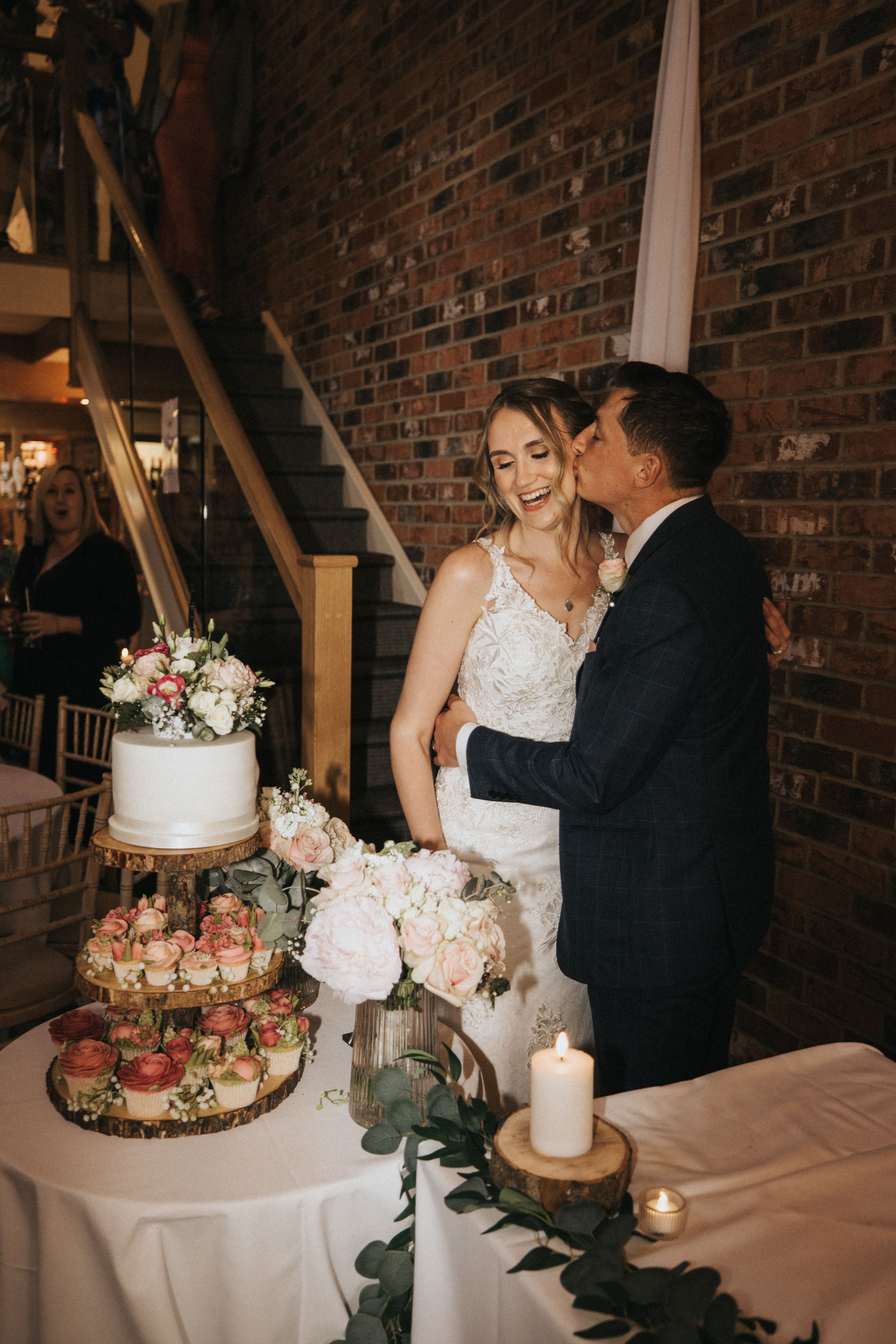 A couple shares an intimate moment beside their elegant three-tiered wedding cake at Hall Farm - image captured by Grimsby photographers.