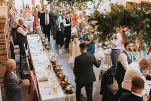 Wedding reception guests mingle around long decorated tables in an elegant indoor venue at Hall Farm - captured by Grimsby photographers.