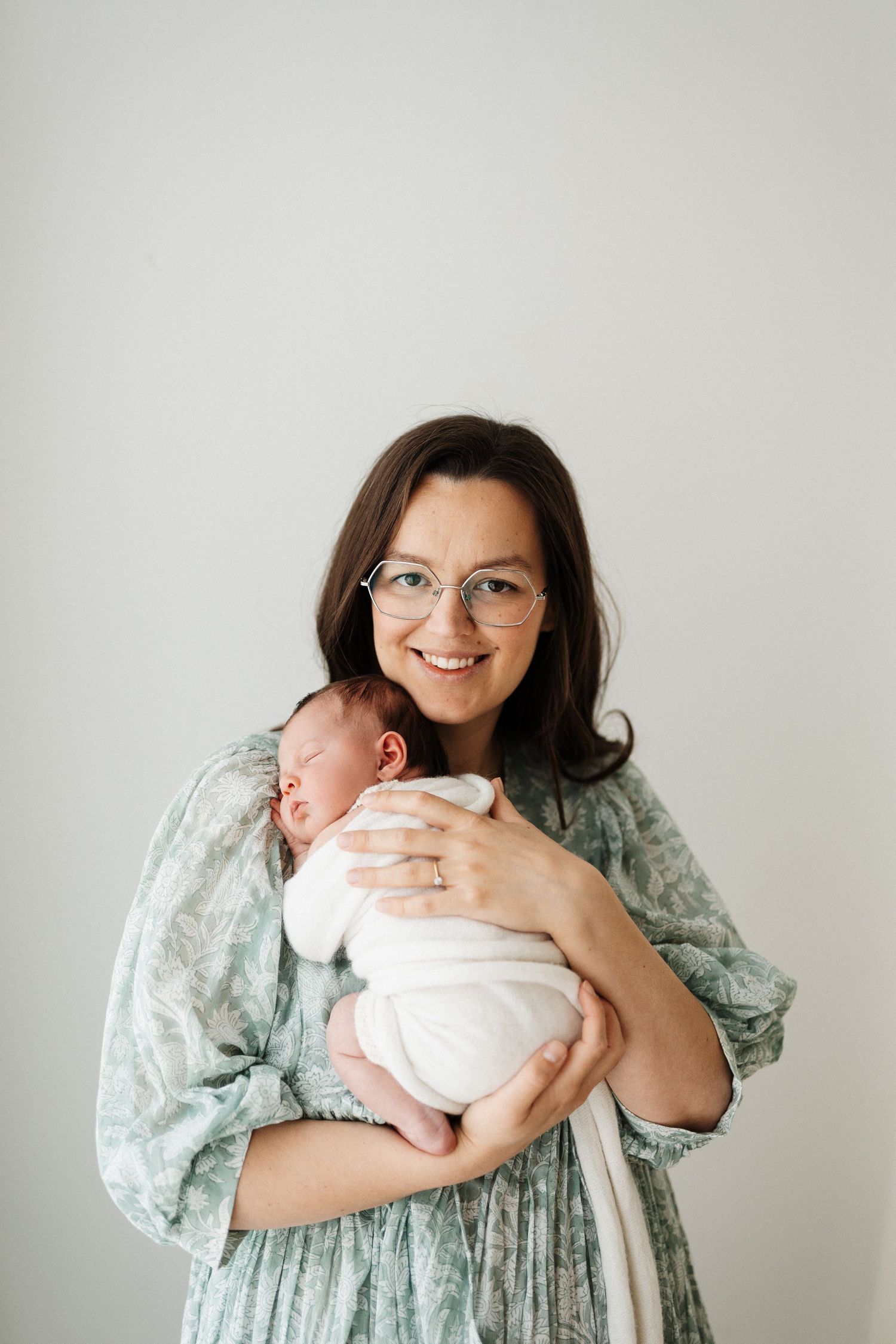 A tender moment between parent and newborn baby in pink fuzzy sweater against white background.