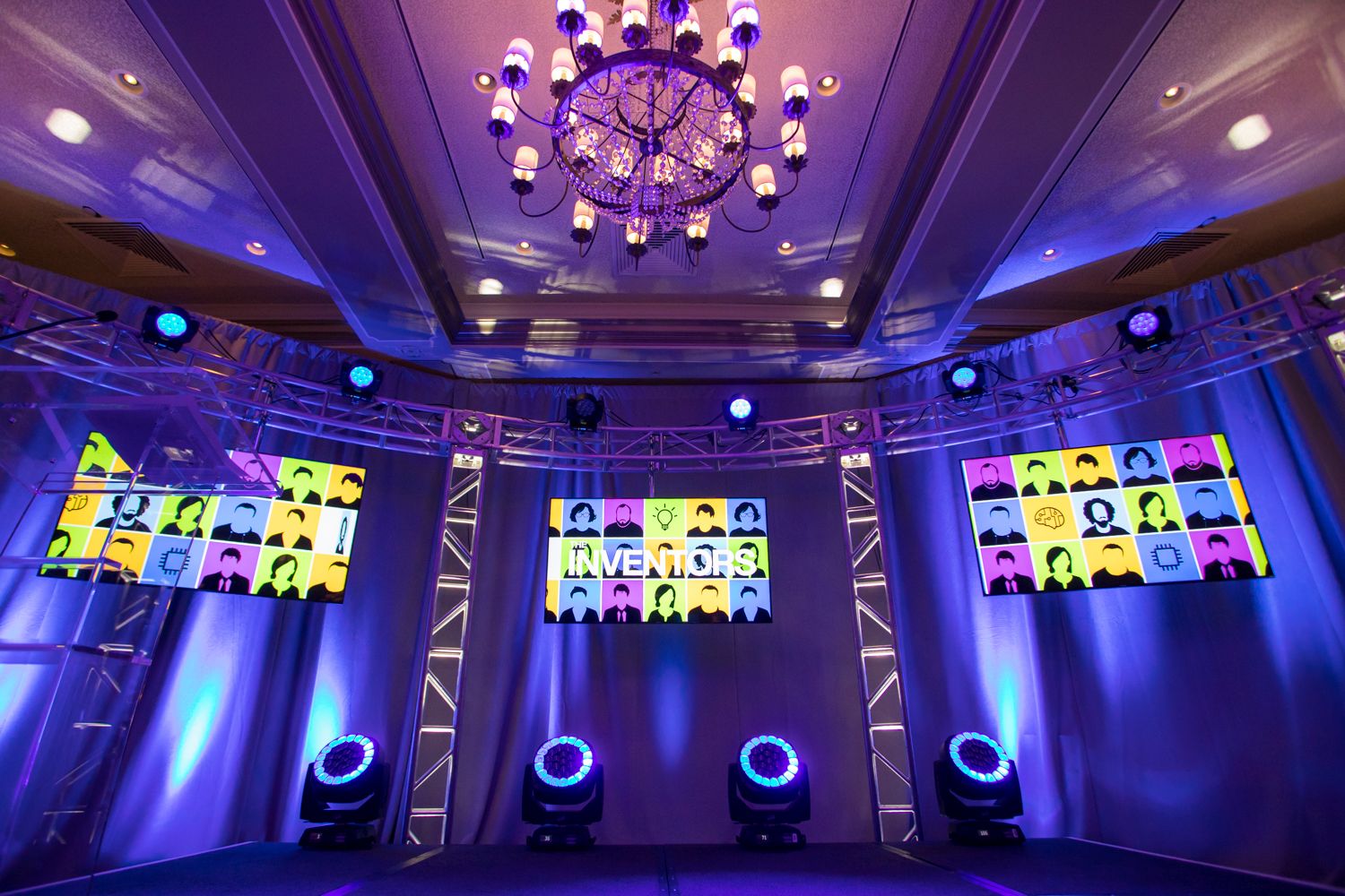 Event venue with purple lighting, multiple LED screens and chandelier creating dramatic atmosphere.