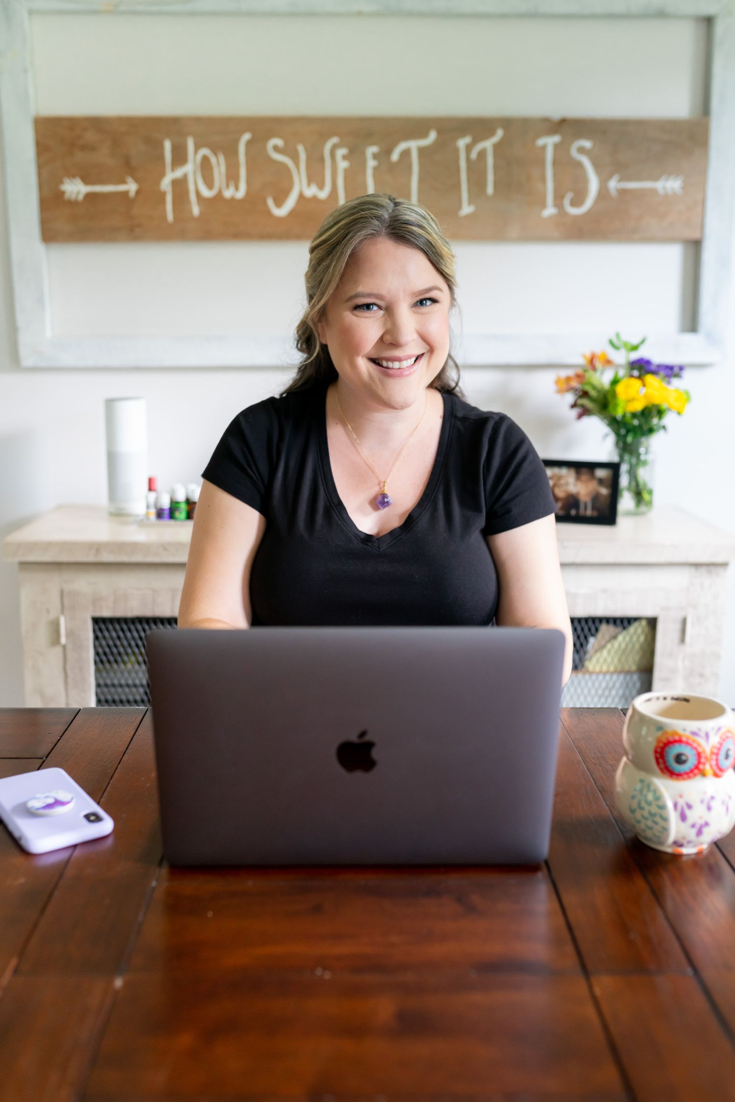 Woman works on laptop at wooden desk under rustic wall sign.