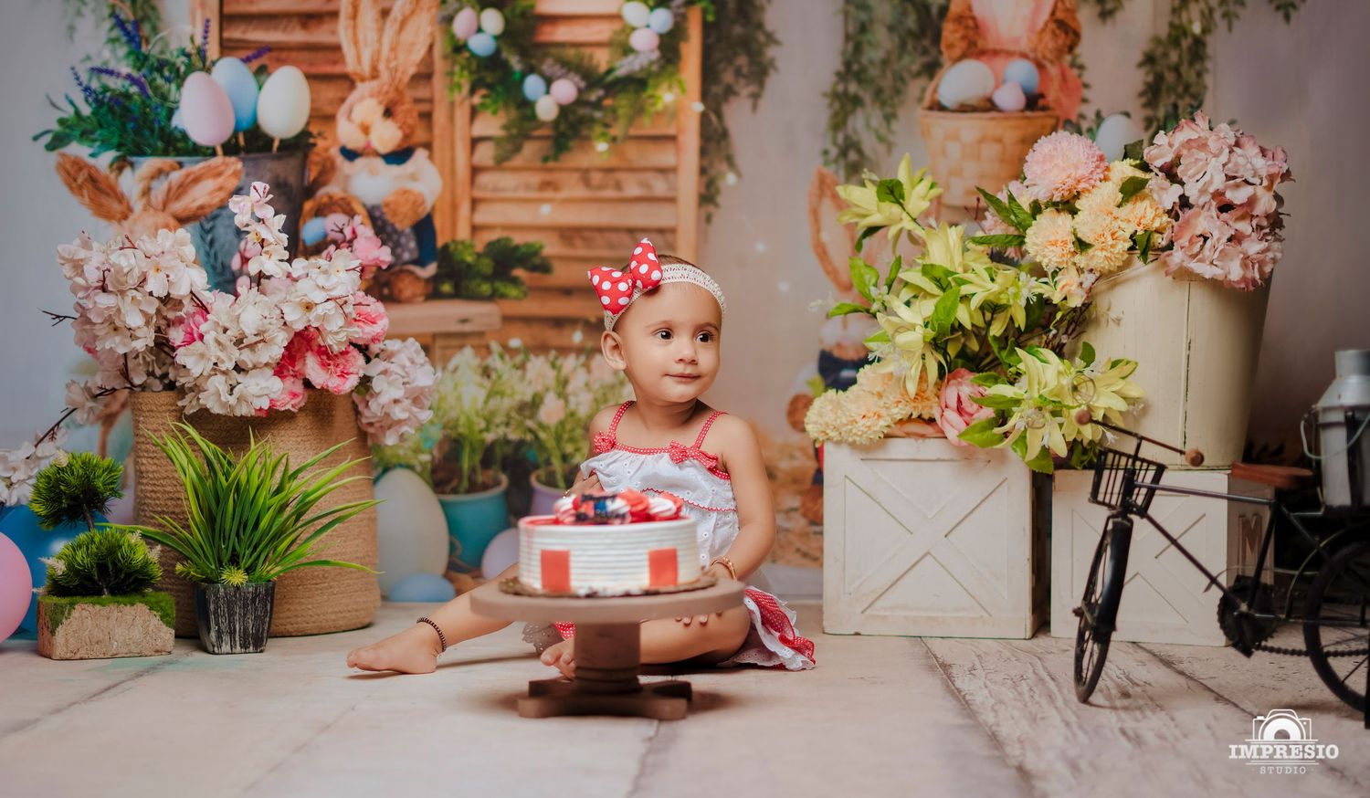 Festive floral setup with cake and decorative elements in pastel colors against wooden backdrop.