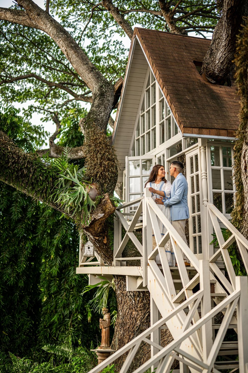 A charming tree house cottage with a white wooden balcony nestled among lush green foliage.