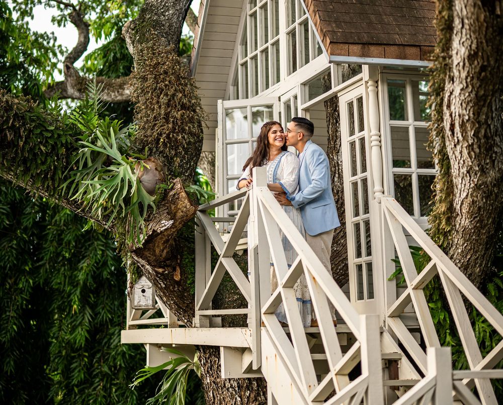 A cozy white tree house with cathedral windows surrounded by tropical greenery on a sunny day.