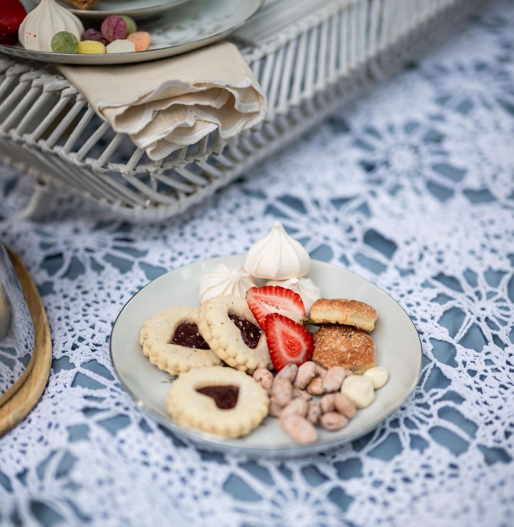 Holiday cookies and pastries displayed on white plates with lace doilies and fresh strawberries.