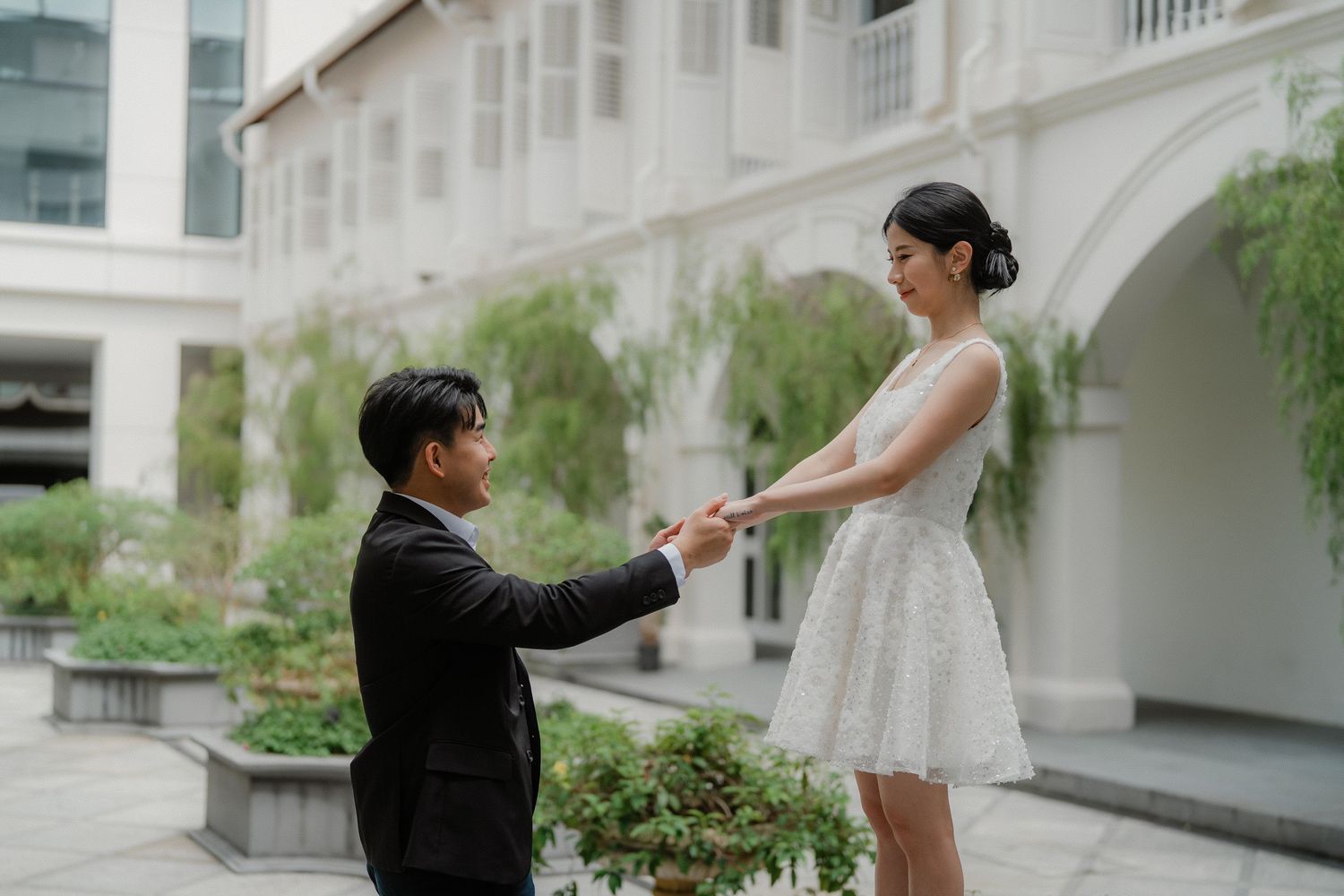 Wedding couple poses playfully in front of a white colonial building with arched windows.