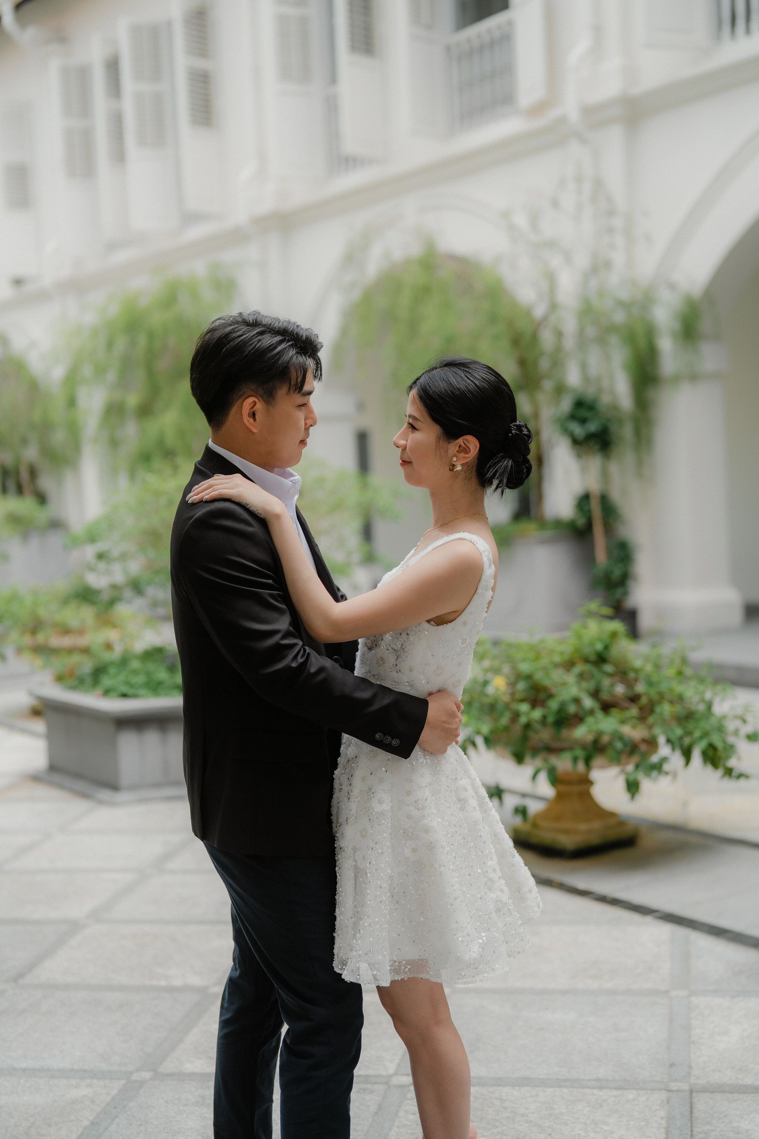 Romantic newlyweds share intimate moments in an elegant white archway corridor with hanging greenery.