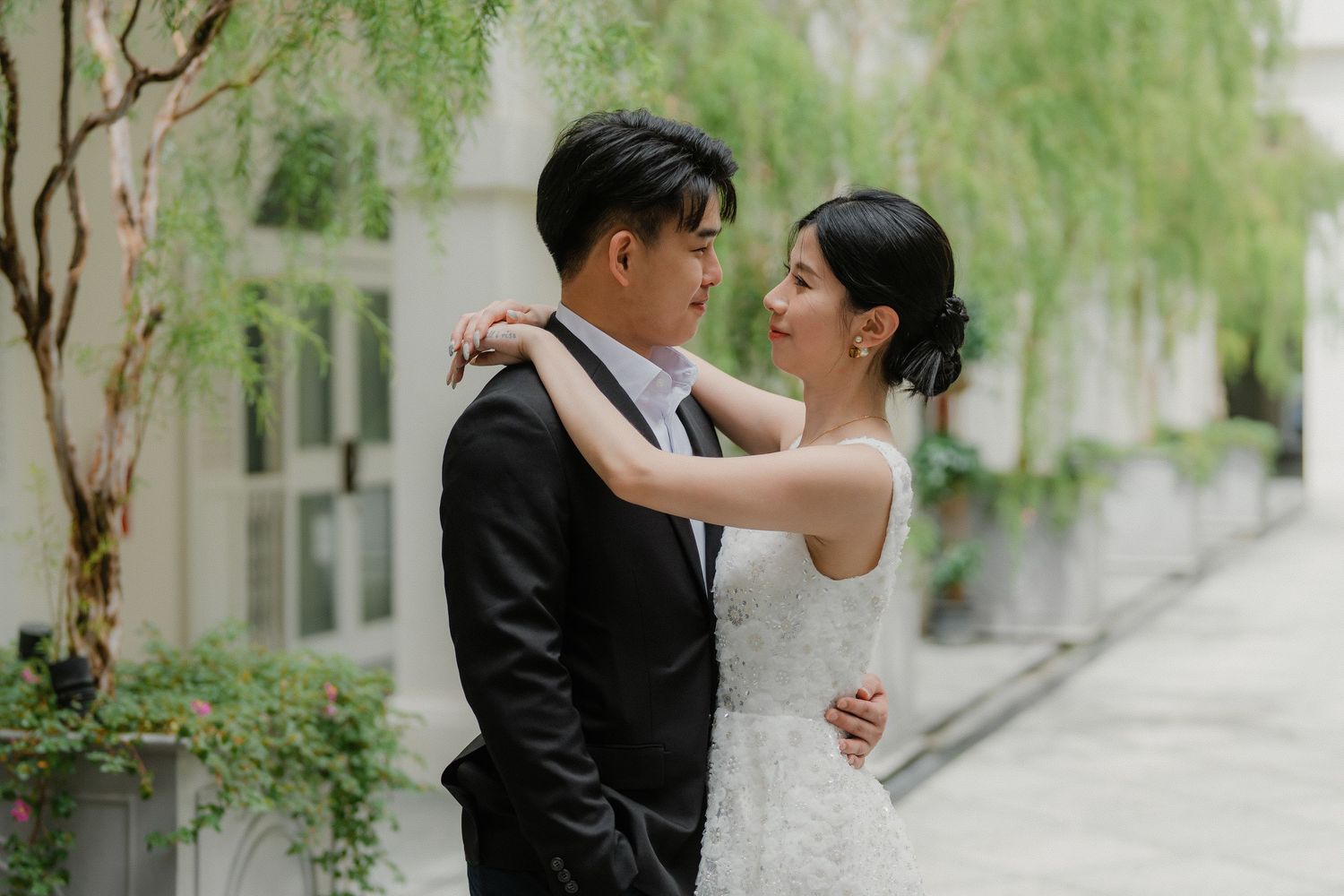 A couple shares an intimate moment under willow trees and stone archways in a romantic garden setting.