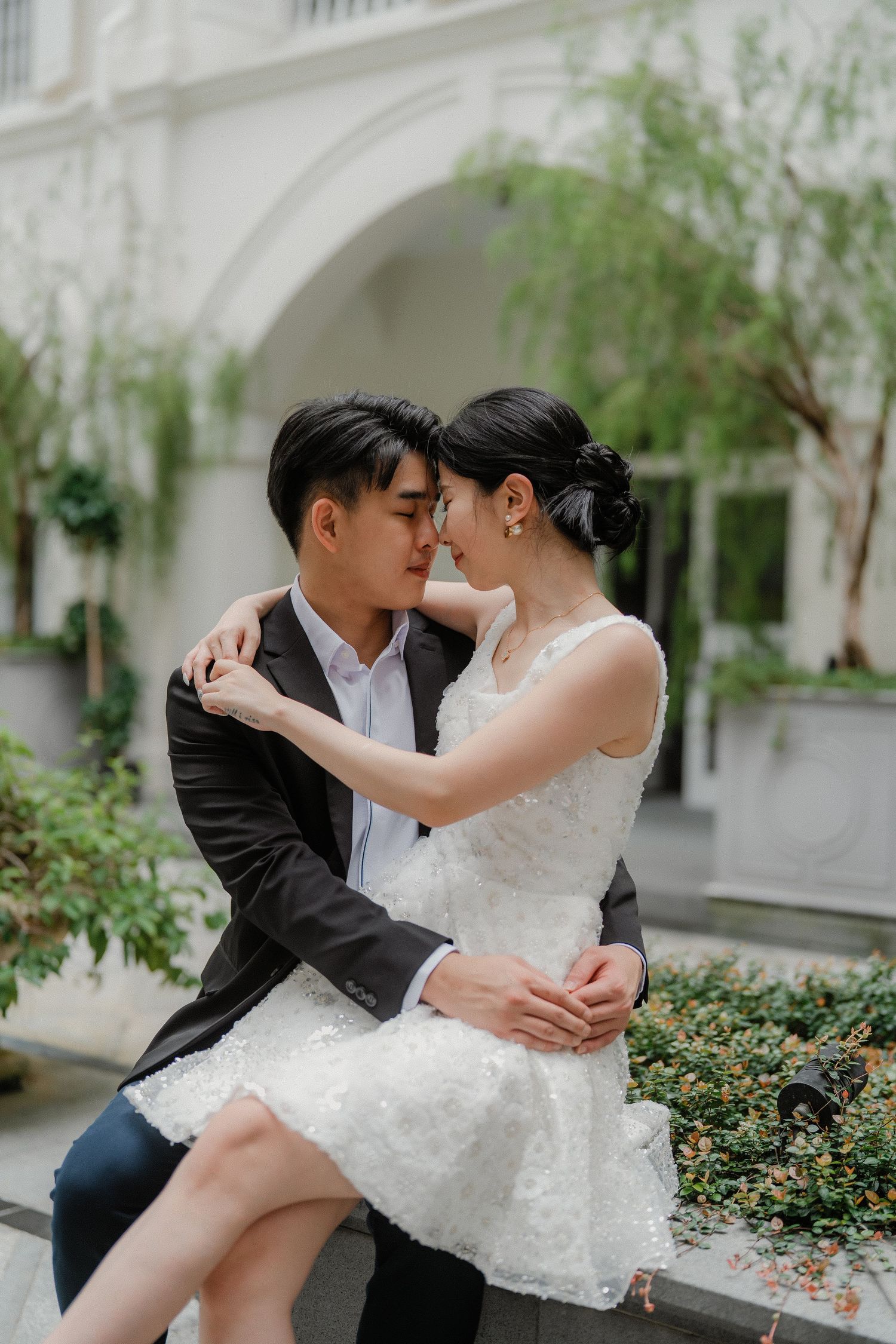 A romantic wedding photo series captured in an elegant courtyard with white architecture and greenery.