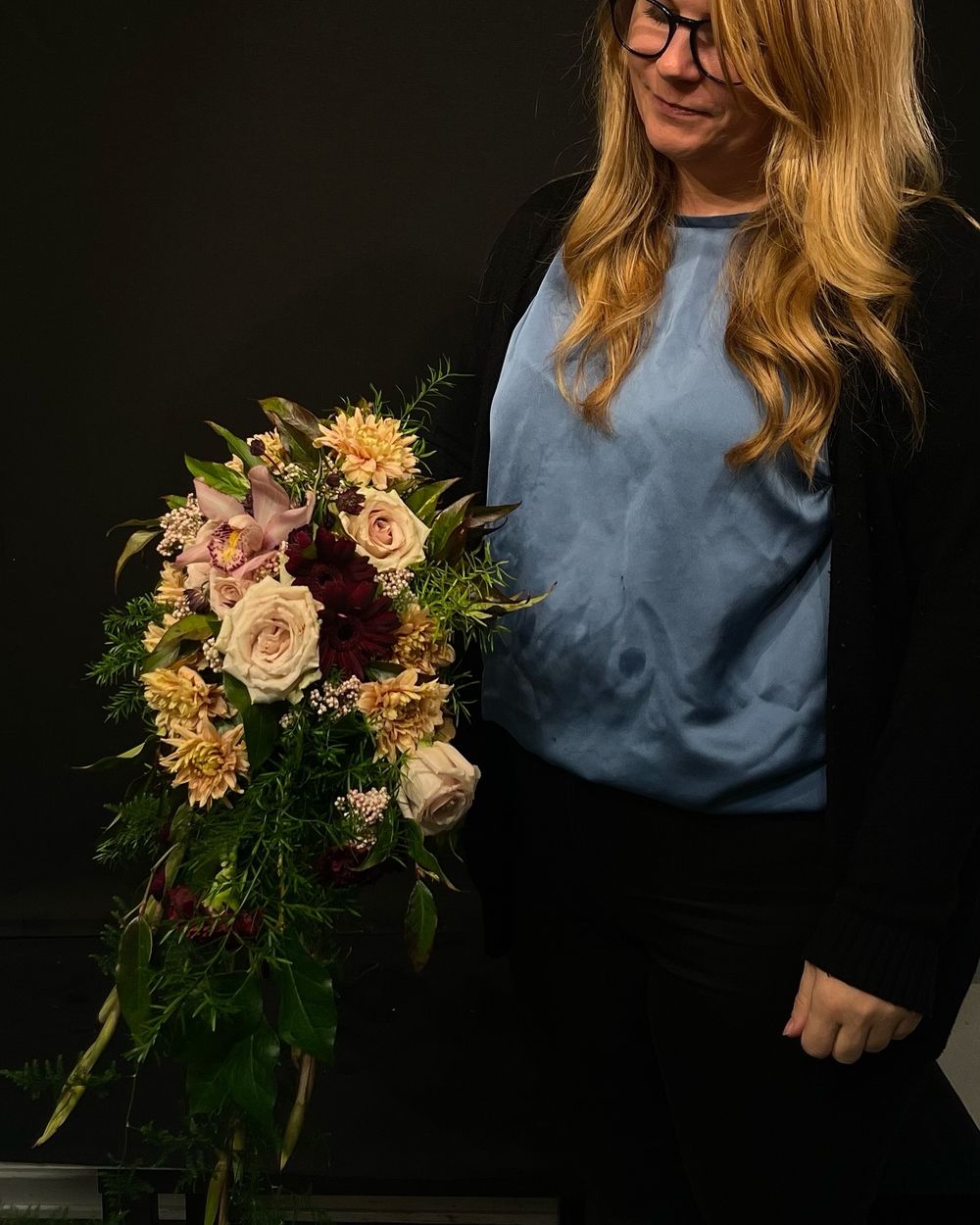Woman with blonde hair holding a cascading bouquet of pink, burgundy, and yellow flowers.