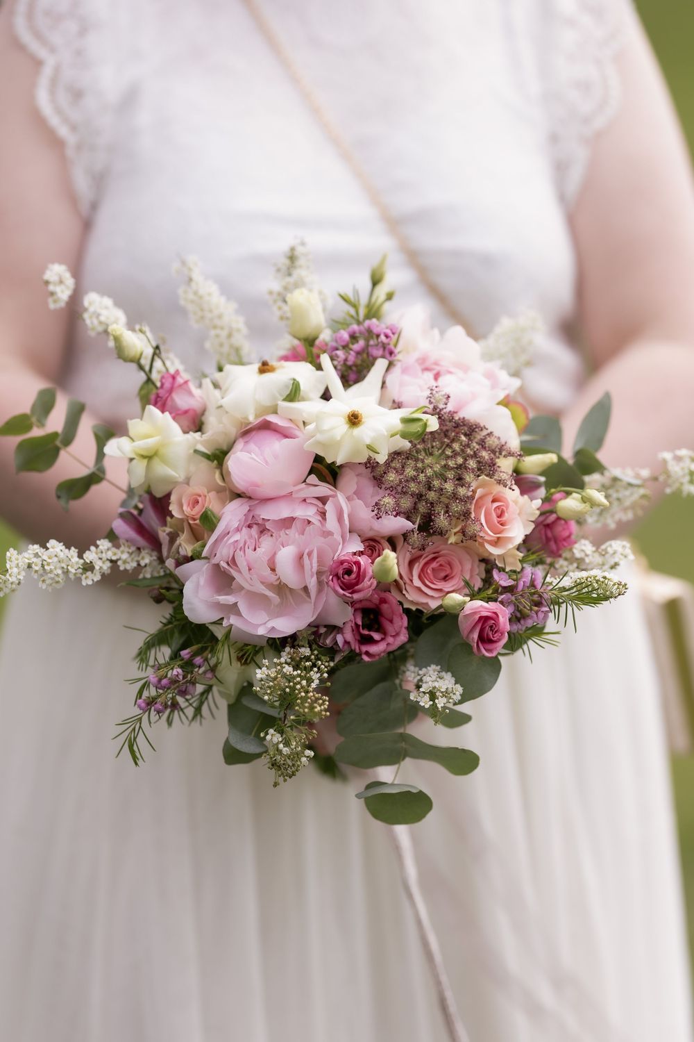 Bride in lace wedding dress holding a lush pink peony and rose bridal bouquet outdoors.