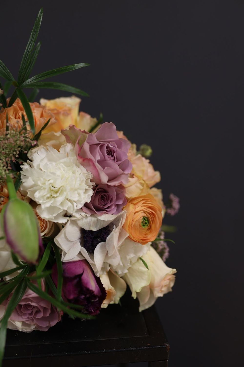 Elegant mixed bouquet with lavender roses, orange ranunculus, white carnations, and dark purple peonies.