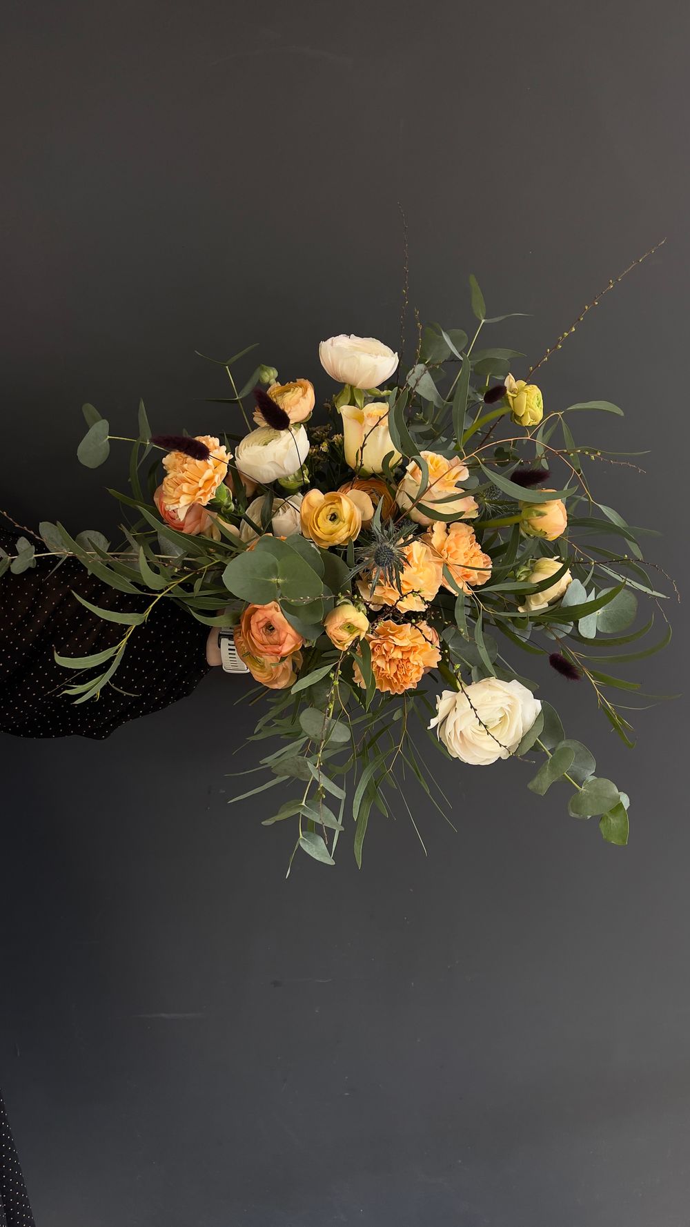 Lush bouquet of orange, yellow, and white roses with eucalyptus greenery against a dark background.