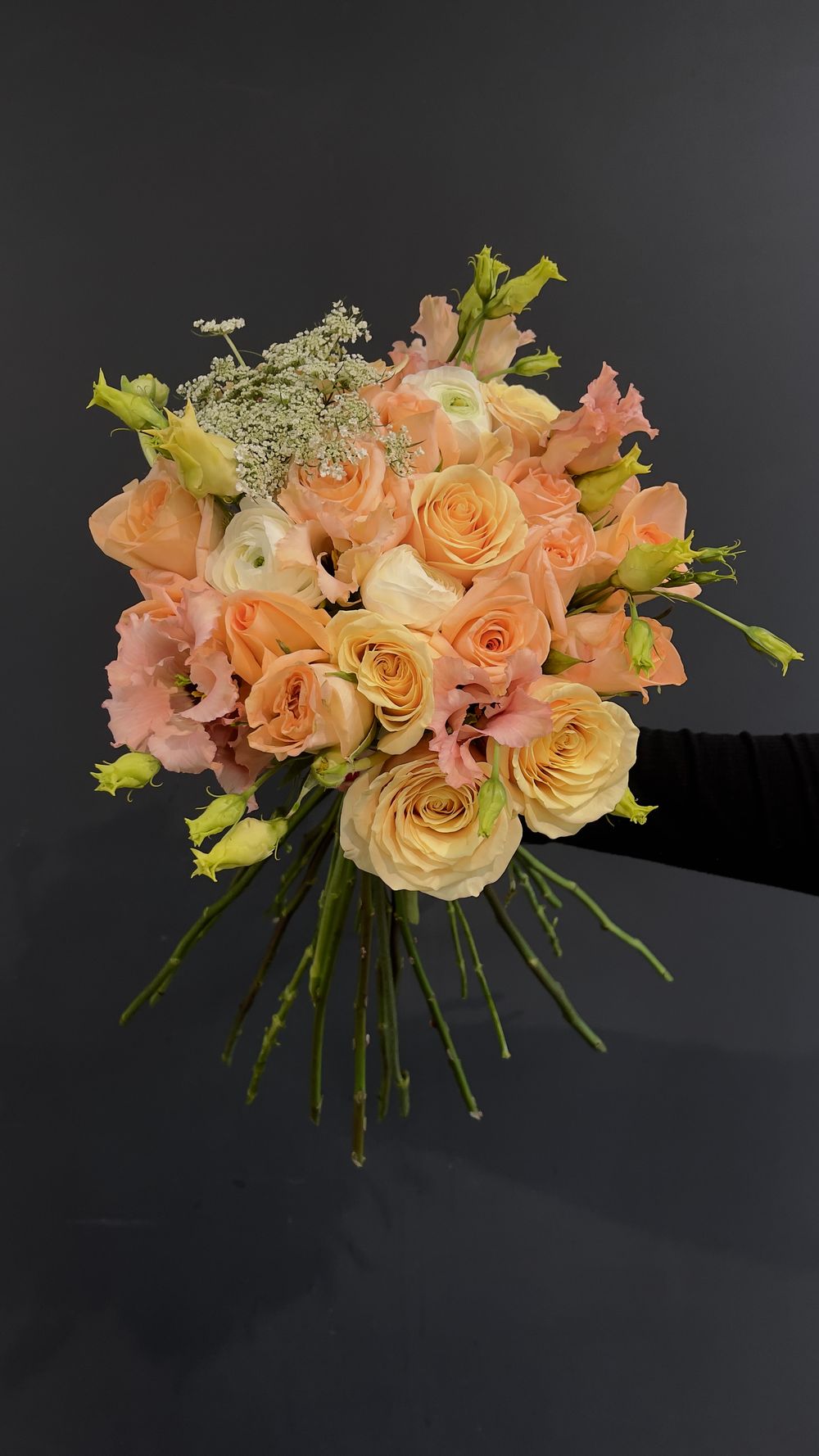 Hand-held peach bridal bouquet with roses, ranunculus, lisianthus, and white Queen Anne's lace filler.