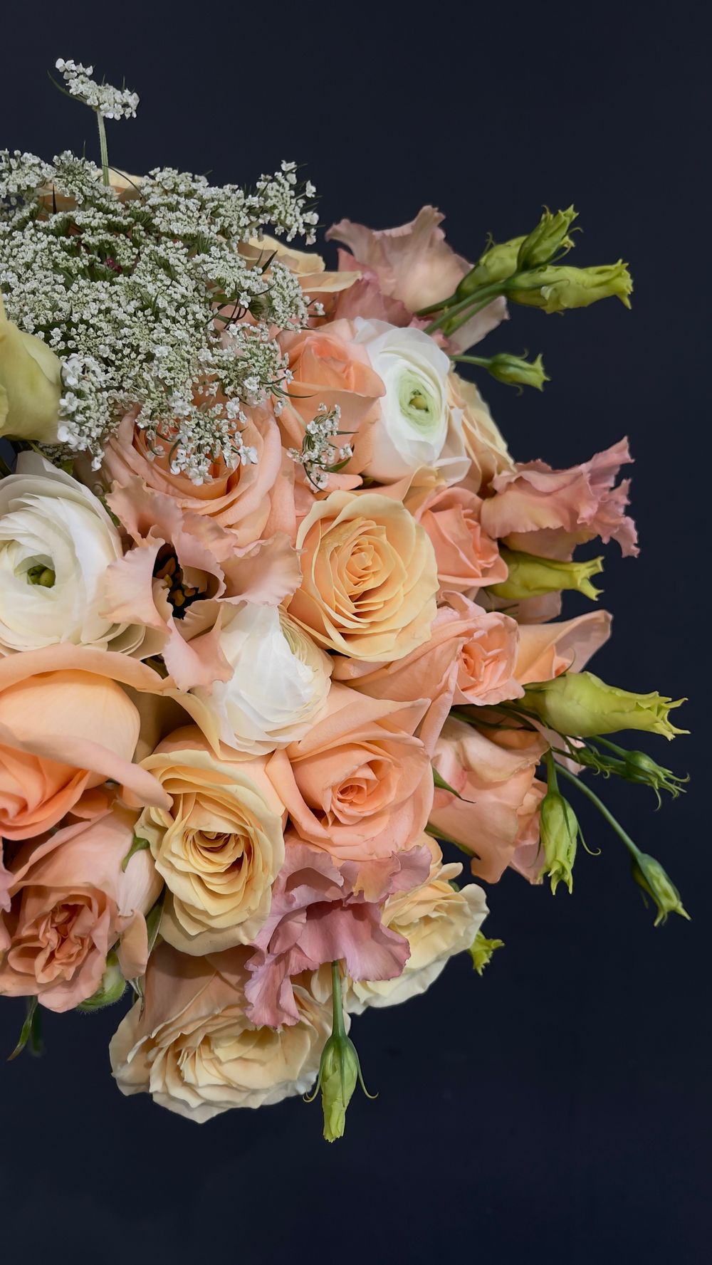 Close-up of a peach bridal bouquet with roses, ranunculus, lisianthus, and delicate white filler flowers.